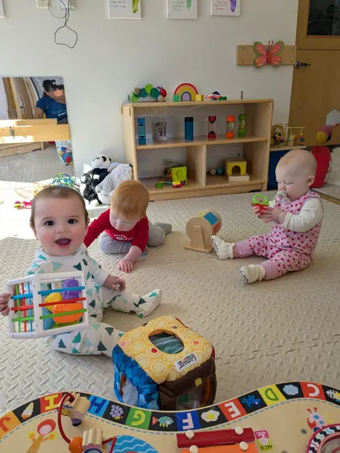 Three infants playing with toys on the floor in the Little Rainbow classroom