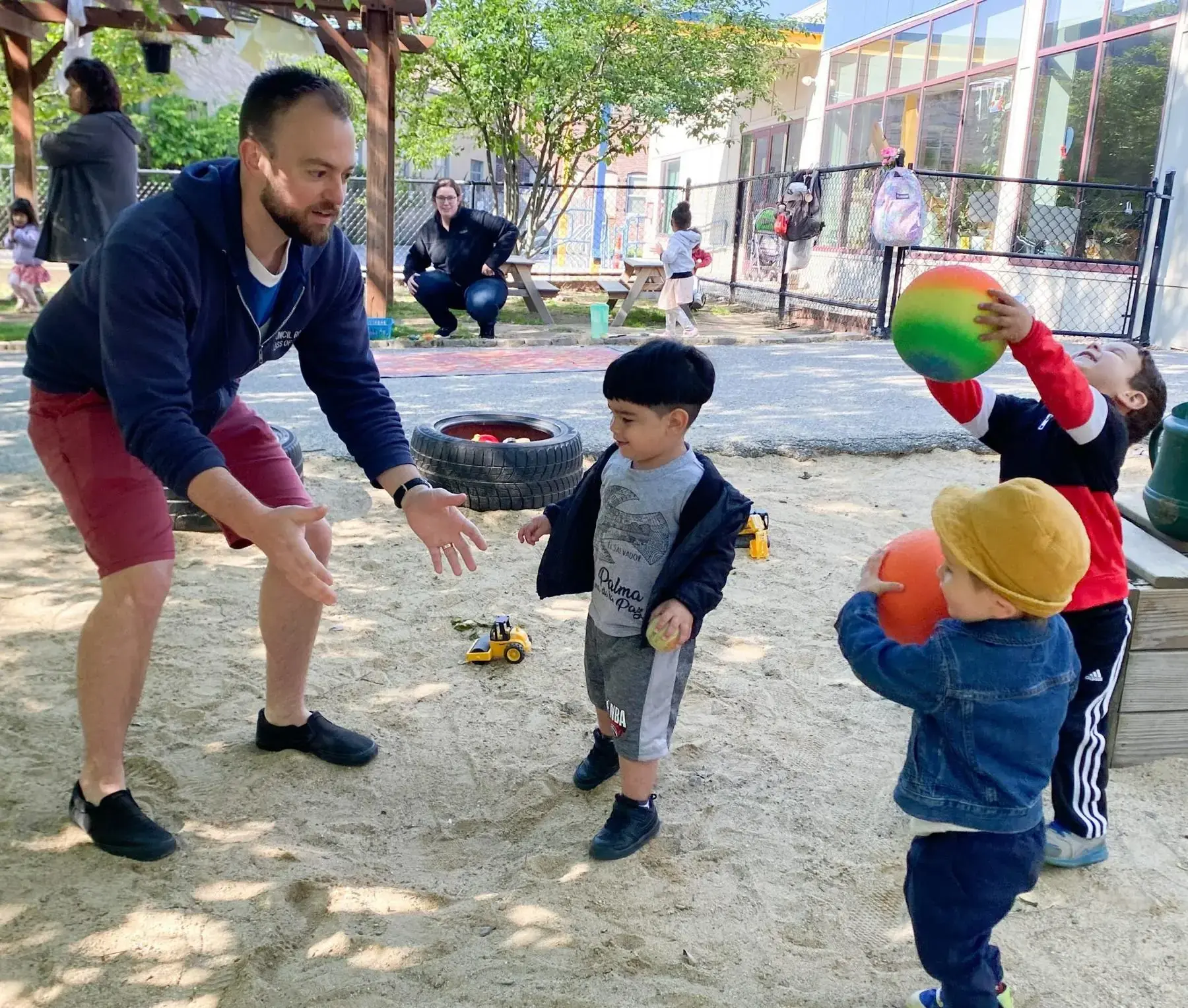 A parent playing ball with children in the Bigelow outdoor playground
