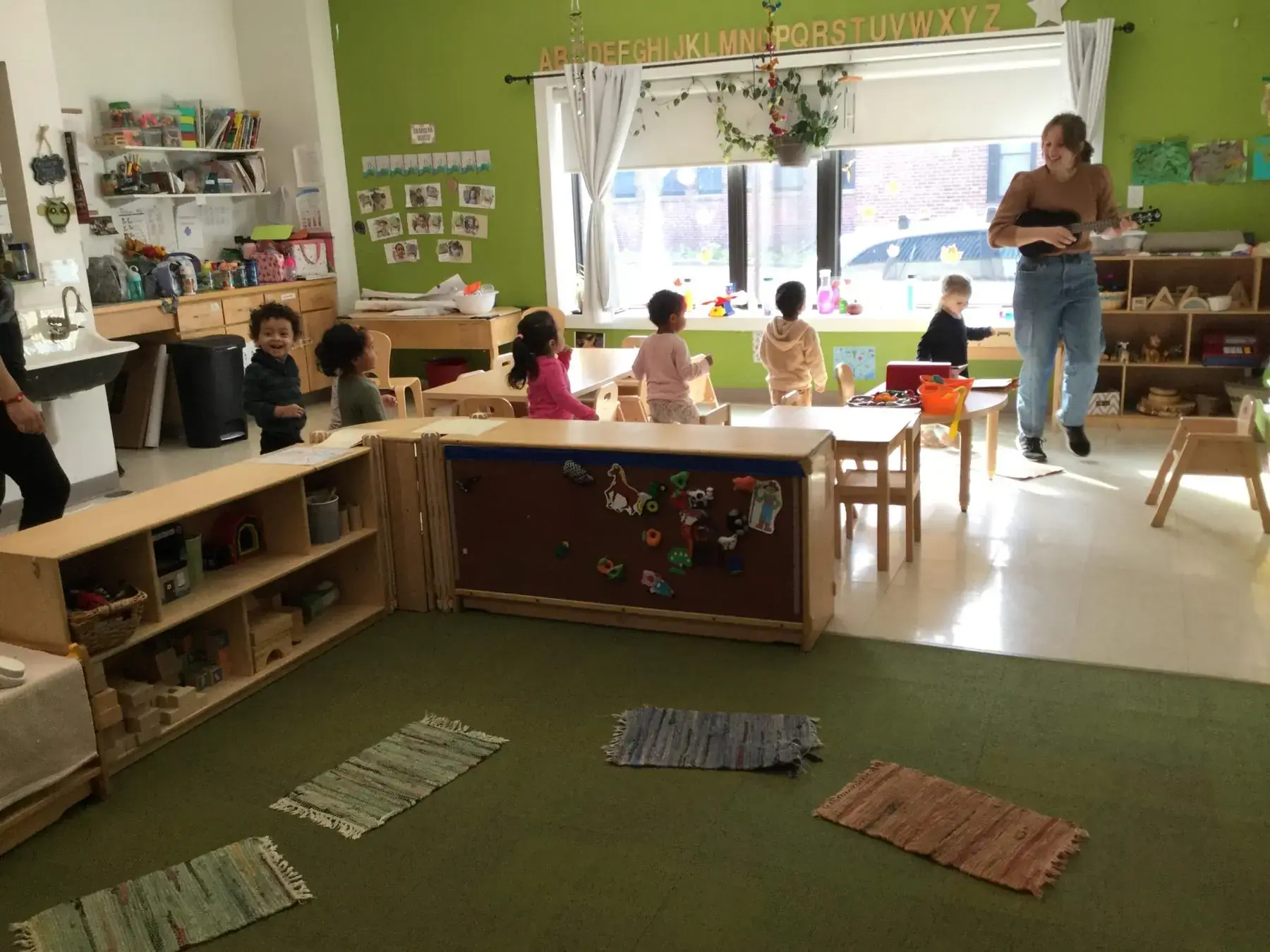 Children and a teacher in the bright green Rainbow 2 classroom