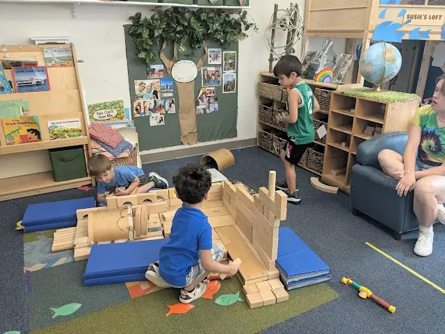 Three preschool children building a fort out of wooden blocks in the Rainbow 3 classroom