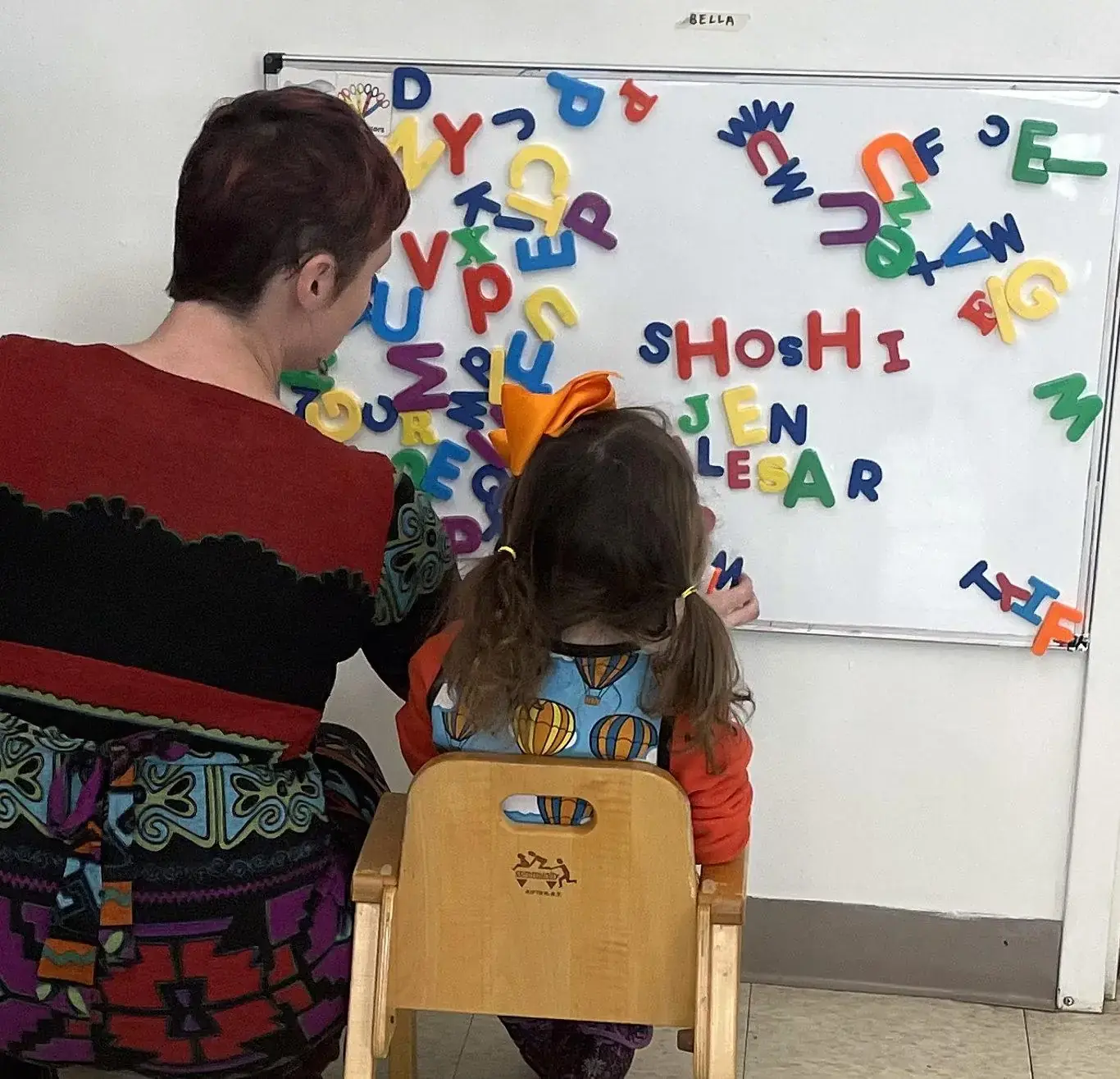 A teacher working with a child on letter recognition at a magnetic letter board